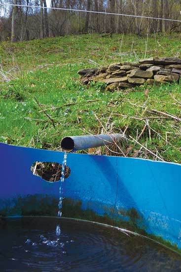 A pipe delivers a small, steady stream of water from a pasture seep to a tank.